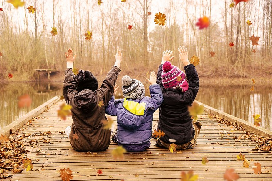 Drei Kinder sitzen auf einem Steg am See und spielen mit Blättern - Copyright: N. Schwarz © GemeindebriefDruckerei.de