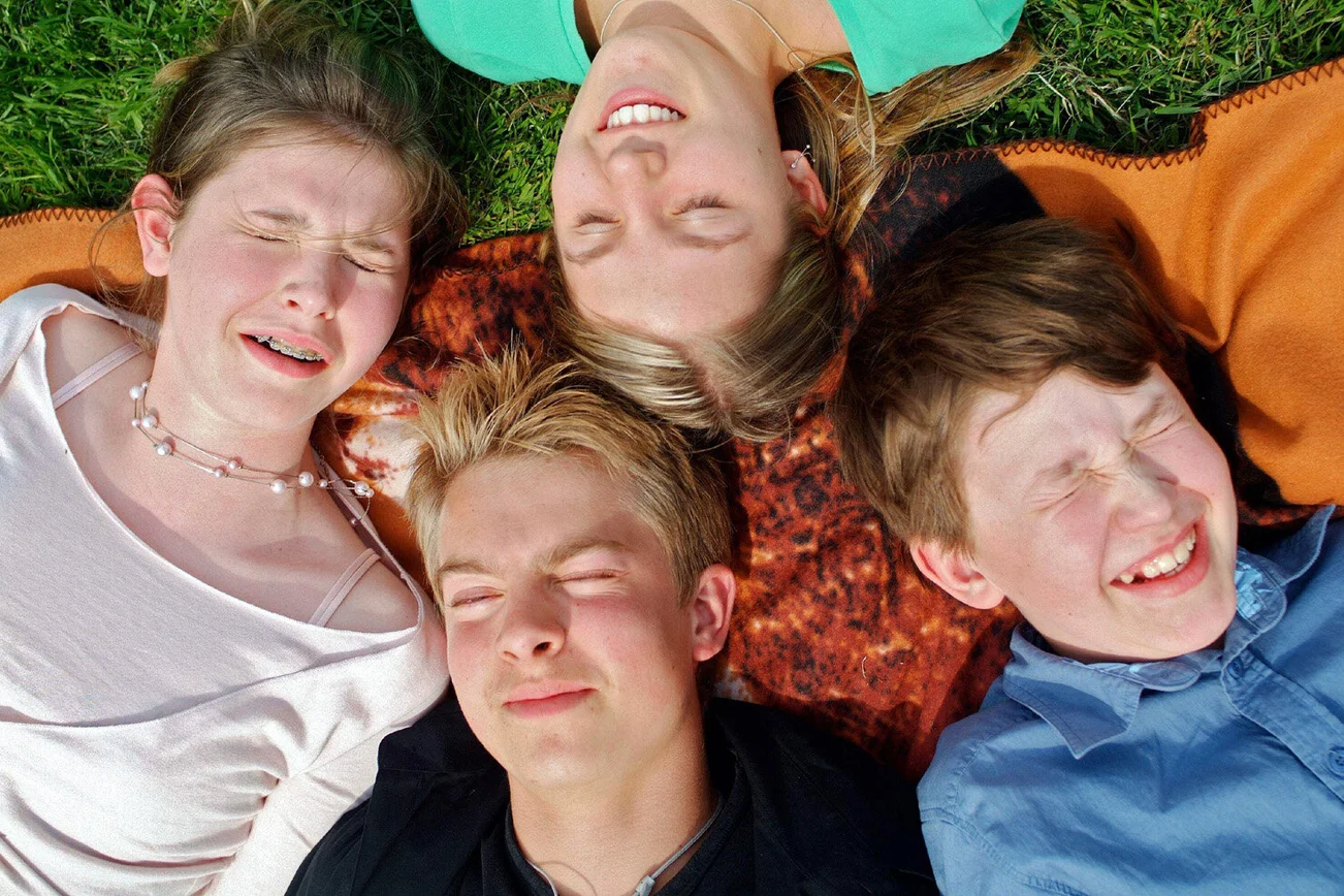 Vier jungen Menschen liegen auf dem Rücken im Gras und schließen die Augen