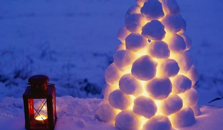 Eine rote Metalllaterne steht im Schnee neben einer Schneeball-Laterne