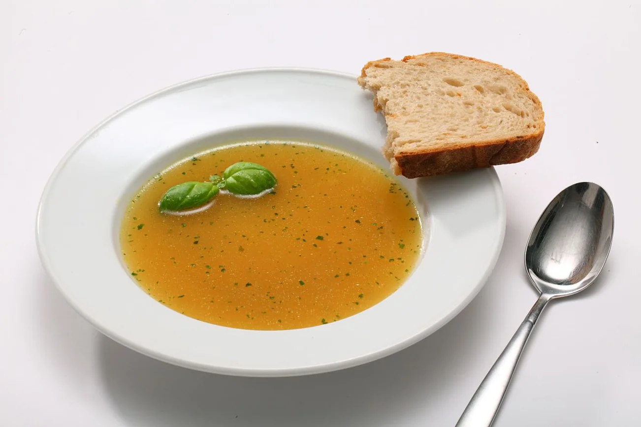 Weißer Suppenteller mit Suppe, Brot und einem Löffel