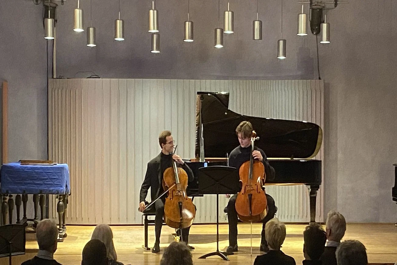 Zwei Chellisten sitzen vor einem Klavier