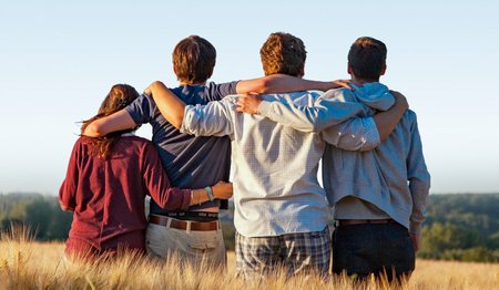 Vier junge Menschen stehen mit dem Rücken zum Betrachter in einem Getreidefeld