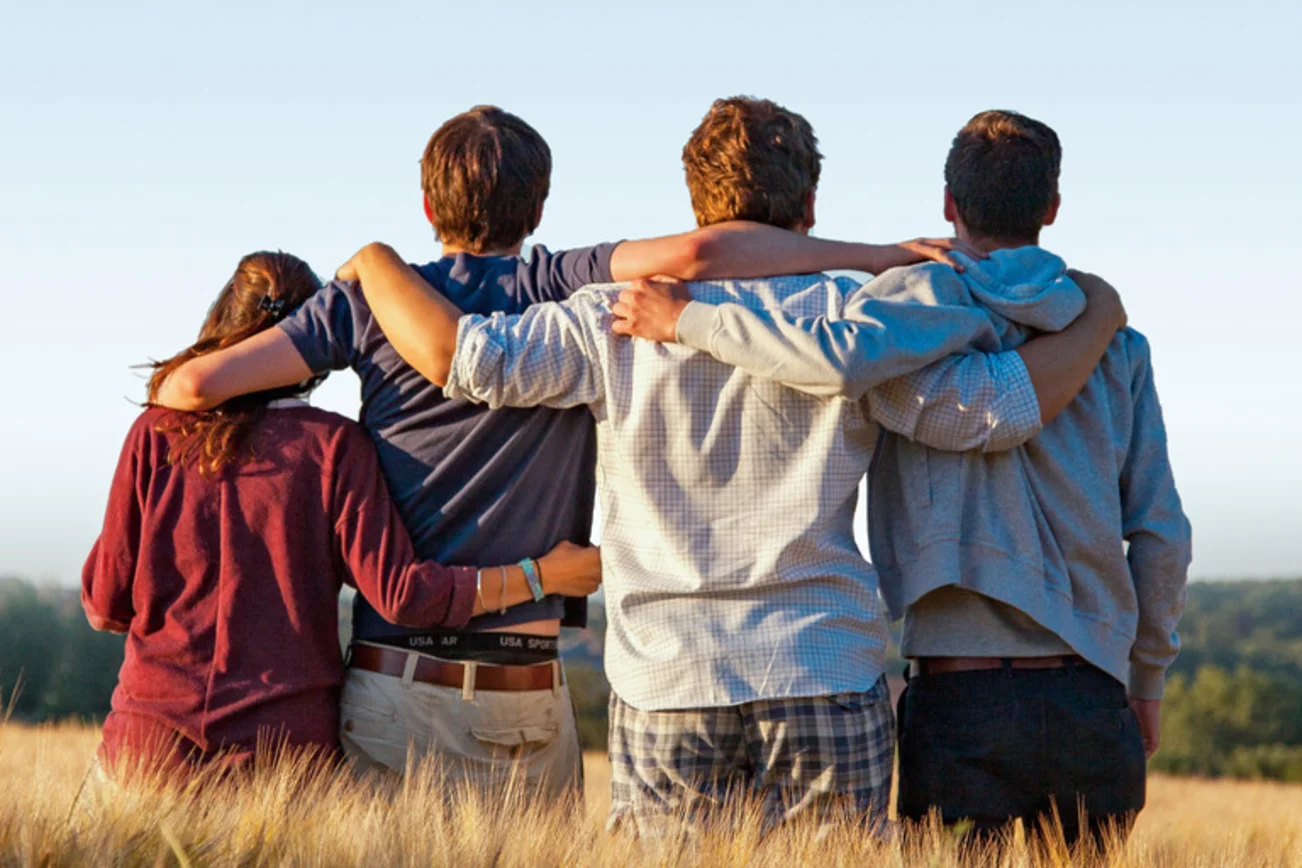 Vier junge Menschen stehen mit dem Rücken zum Betrachter in einem Getreidefeld