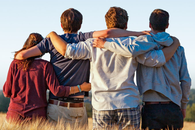 Vier junge Menschen stehen mit dem Rücken zum Betrachter in einem Getreidefeld