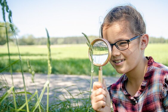Kind mit Brille sieht durch ein Vergrößerungsglas - Copyright:  N. Schwarz © GemeindebriefDruckerei.de