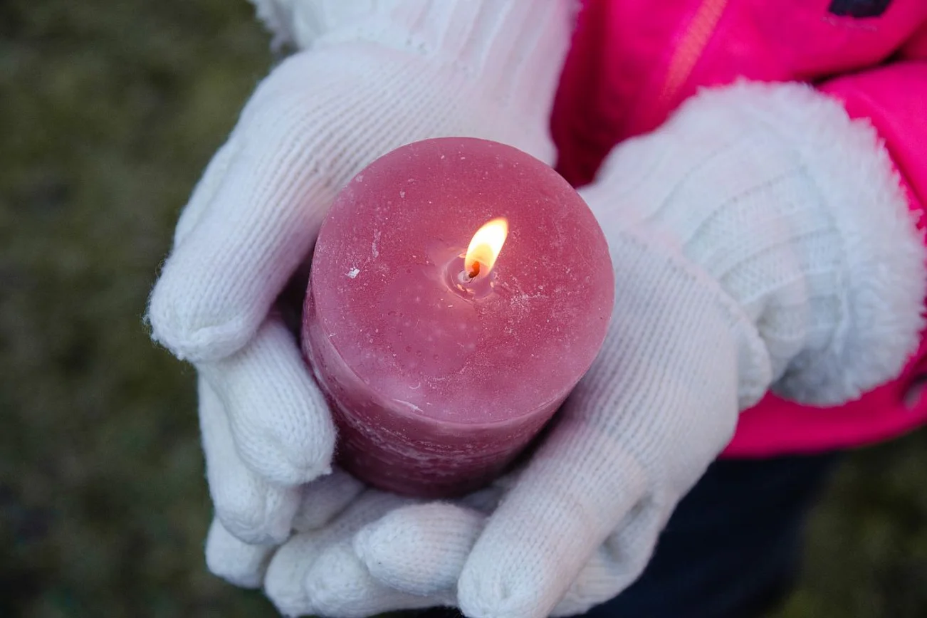 Zwei Hände in weißen Handschuhen tragen eine brennende, rosa Kerze