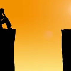 Eine Person sitz vor einer schwarzen Schlucht. Rechts im Bild scheint die Sonne durch einen orangefarbenen Hintergrund.
