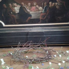 Dornenkranz mit Blüten auf dem Altar vor einem Bild vom Abendmahl