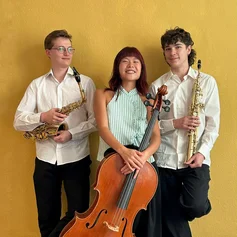 Drei junge Musiker stehen mit ihren Instrumenten vor einer gelben Wand