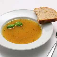 Weißer Suppenteller mit Suppe, Brot und einem Löffel