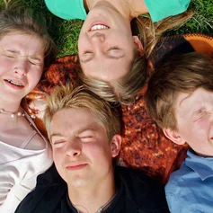 Vier jungen Menschen liegen auf dem Rücken im Gras und schließen die Augen