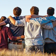 Vier junge Menschen stehen mit dem Rücken zum Betrachter in einem Getreidefeld